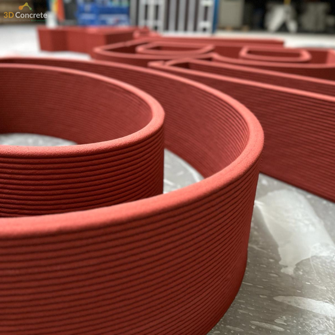 <img src="https://3dconcrete.fr/actualites/un-nouveau-projet-urbain-en-impression-3d-beton/urbansuspense.jpg" alt="textured detail of a urban structure printed in red concrete by 3D Concrete, a concrete 3D printing company.">