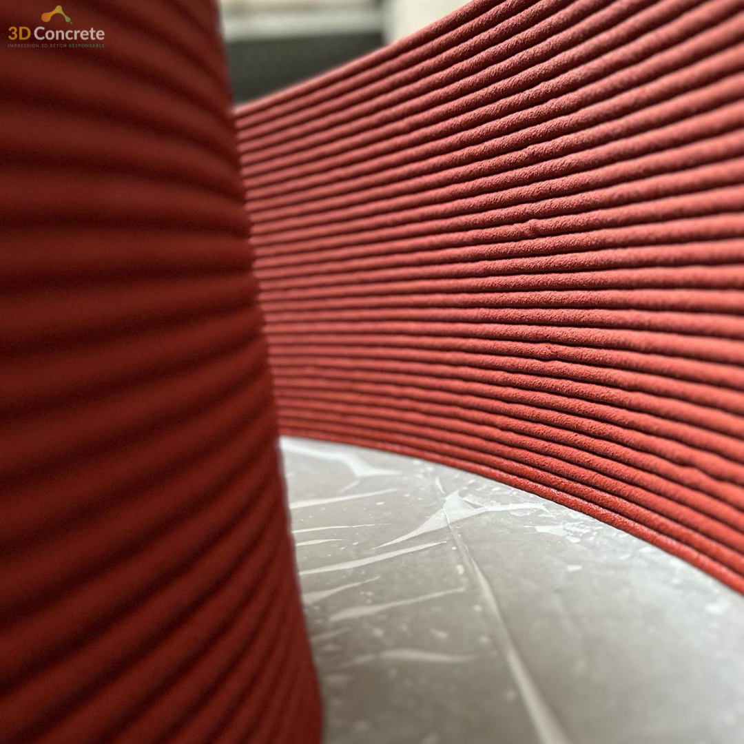 <img src="https://3dconcrete.fr/actualites/un-nouveau-projet-urbain-en-impression-3d-beton/urbansuspense.jpg" alt="textured detail of a urban structure printed in red concrete by 3D Concrete, a concrete 3D printing company.">